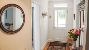 A hallway with a white door, a mirror, a rug, and a vase with flowers. - The Keel Row (Salcombe)