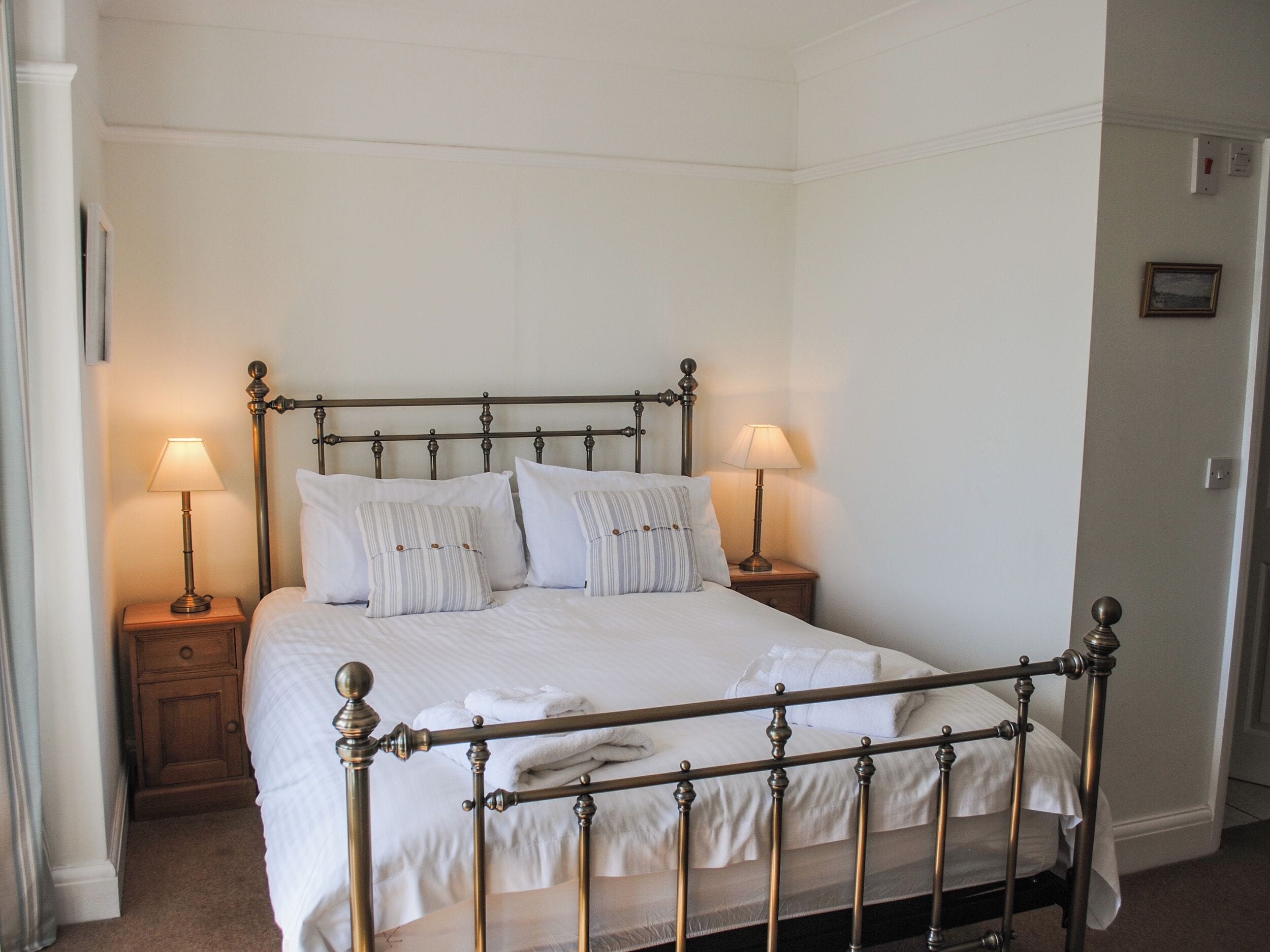 A neatly made bed with white linens and striped pillows, two bedside lamps, and a wooden nightstand.