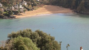 A coastal area with a sandy beach, clear water, and houses on a hillside. - The Keel Row (Salcombe)