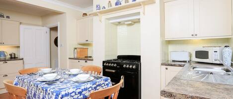 A kitchen with a dining table set for four, a stove, microwave, and a sink.