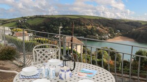 A table set with white and blue patterned plates, cups, and a teapot, overlooking a coastal landscape with hills and a beach. - The Keel Row (Salcombe)