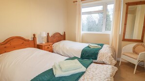 Een slaapkamer met twee bedden, een nachtkastje, een stoel en een raam met gordijnen.
