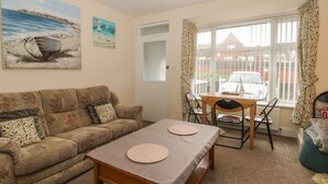 A cozy living room with a sofa, a coffee table, and a dining table with chairs. There are two paintings on the wall, a window with curtains, and a radiator. - Helredale Retreat Whitby (Whitby)