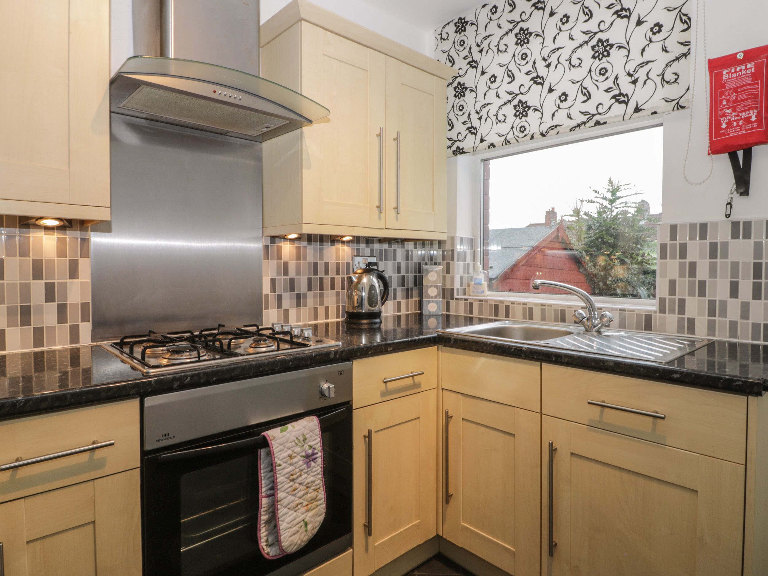 A modern kitchen with a gas stove, oven, stainless steel range hood, and a window with a view of the outside.