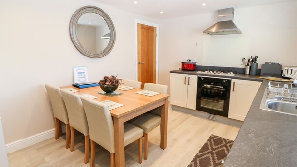 A compact kitchen with a dining area, featuring a wooden table, chairs, a modern oven, and a stainless steel range hood.