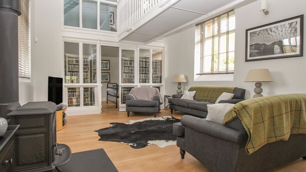 A spacious living room with a high ceiling, a fireplace, a large window, and a cozy seating area.