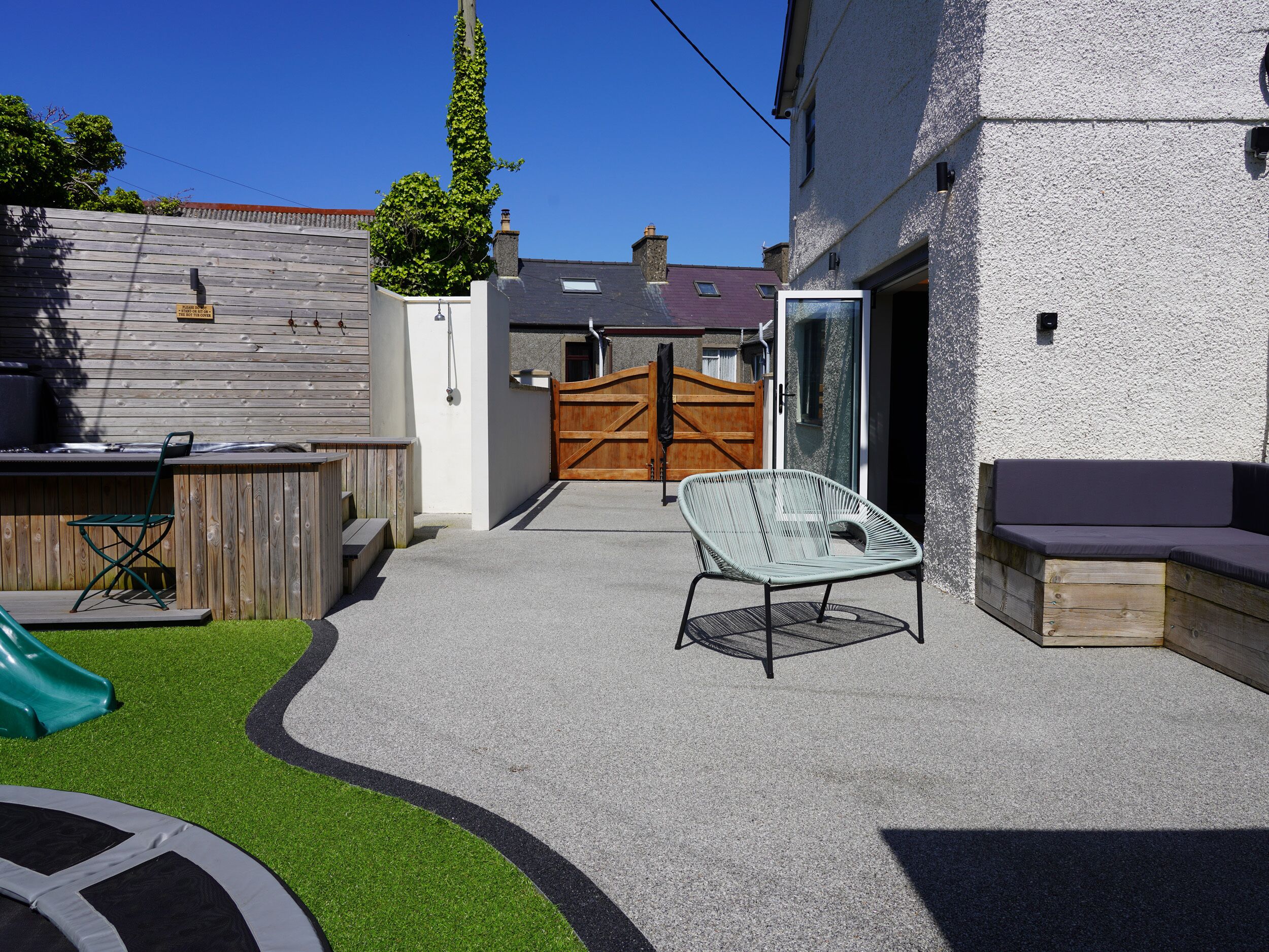 Un jardin avec une terrasse en bois, une chaise verte, un banc et un toboggan.