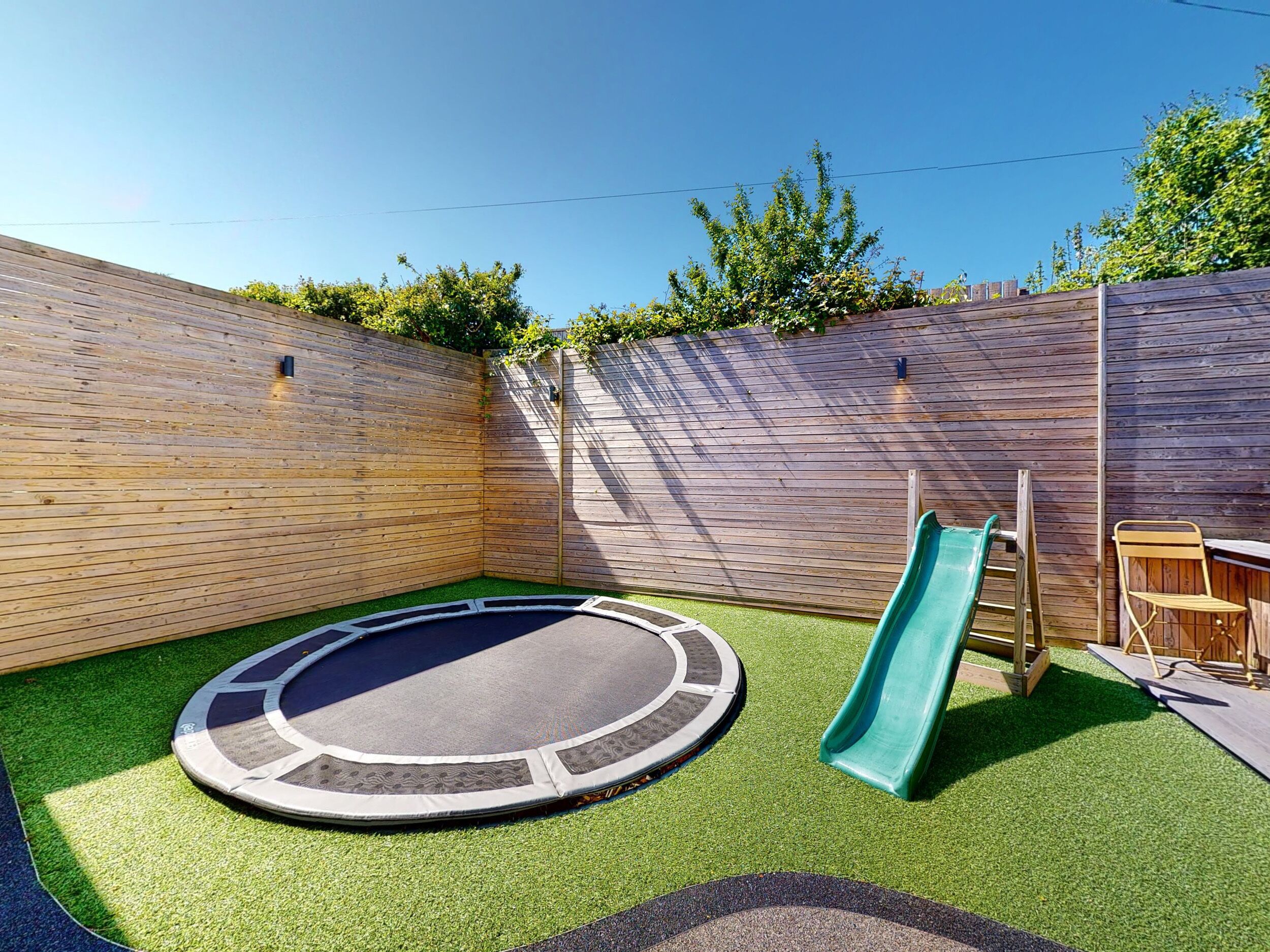Un patio trasero con un trampolín, un tobogán y una valla de madera.