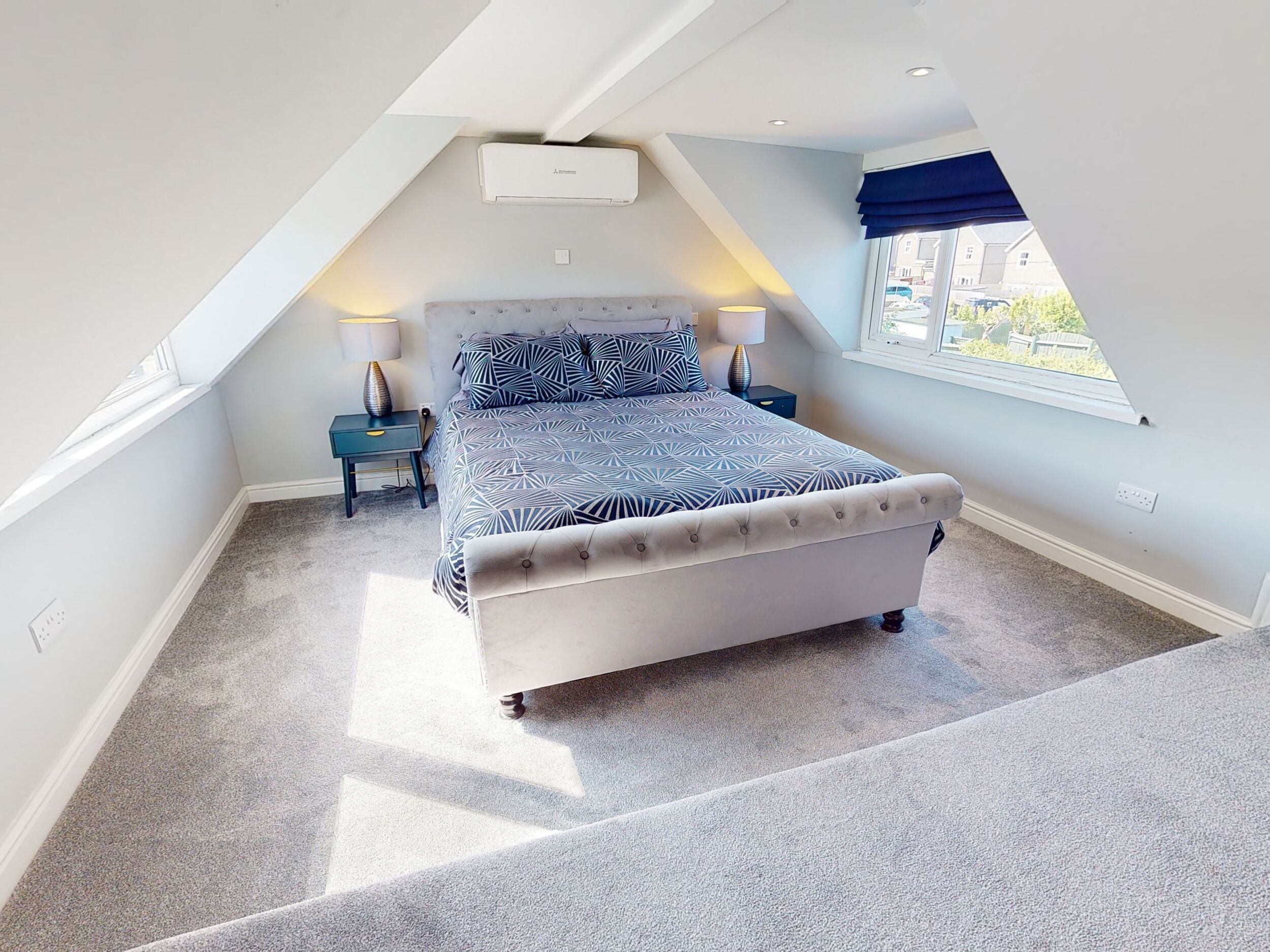 A bedroom with a bed, two bedside tables, a window, and an air conditioning unit.