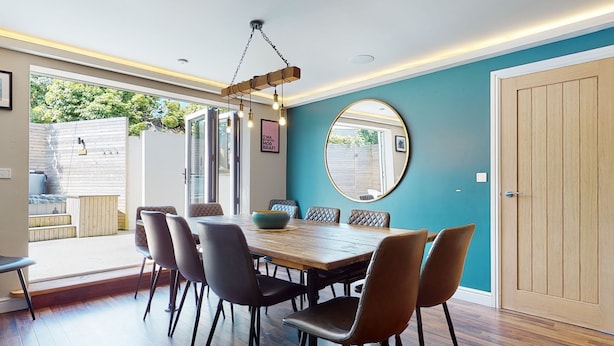 Uma sala de jantar com mesa e cadeiras de madeira, um lustre pendente e um espelho grande na parede.