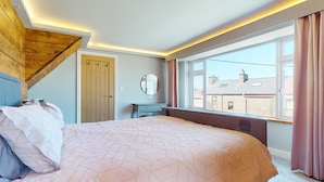 Quarto com cama, penteadeira, espelho e janela com cortinas.
