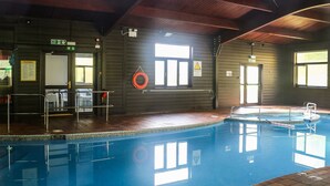 Une piscine intérieure dotée d’une terrasse en bois, d’une bouée de sauvetage et d’un panneau indiquant les règles de la piscine.