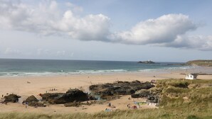 A beach with rocky outcrops, a lighthouse, and a small white building. - Miles Retreat (Hayle)
