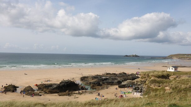 Une plage avec des affleurements rocheux, un phare et un petit bâtiment blanc.
