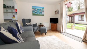 Un salon avec un canapé gris, un fauteuil, un téléviseur posé sur un meuble en bois et un tableau accroché au mur.