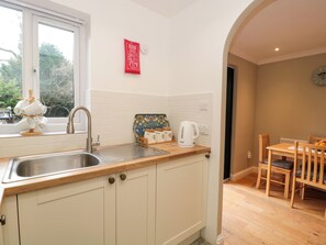 A compact kitchen with a sink, a kettle, and a window. There is a dining area with a table and chairs. - The Seventeen (Cheltenham)