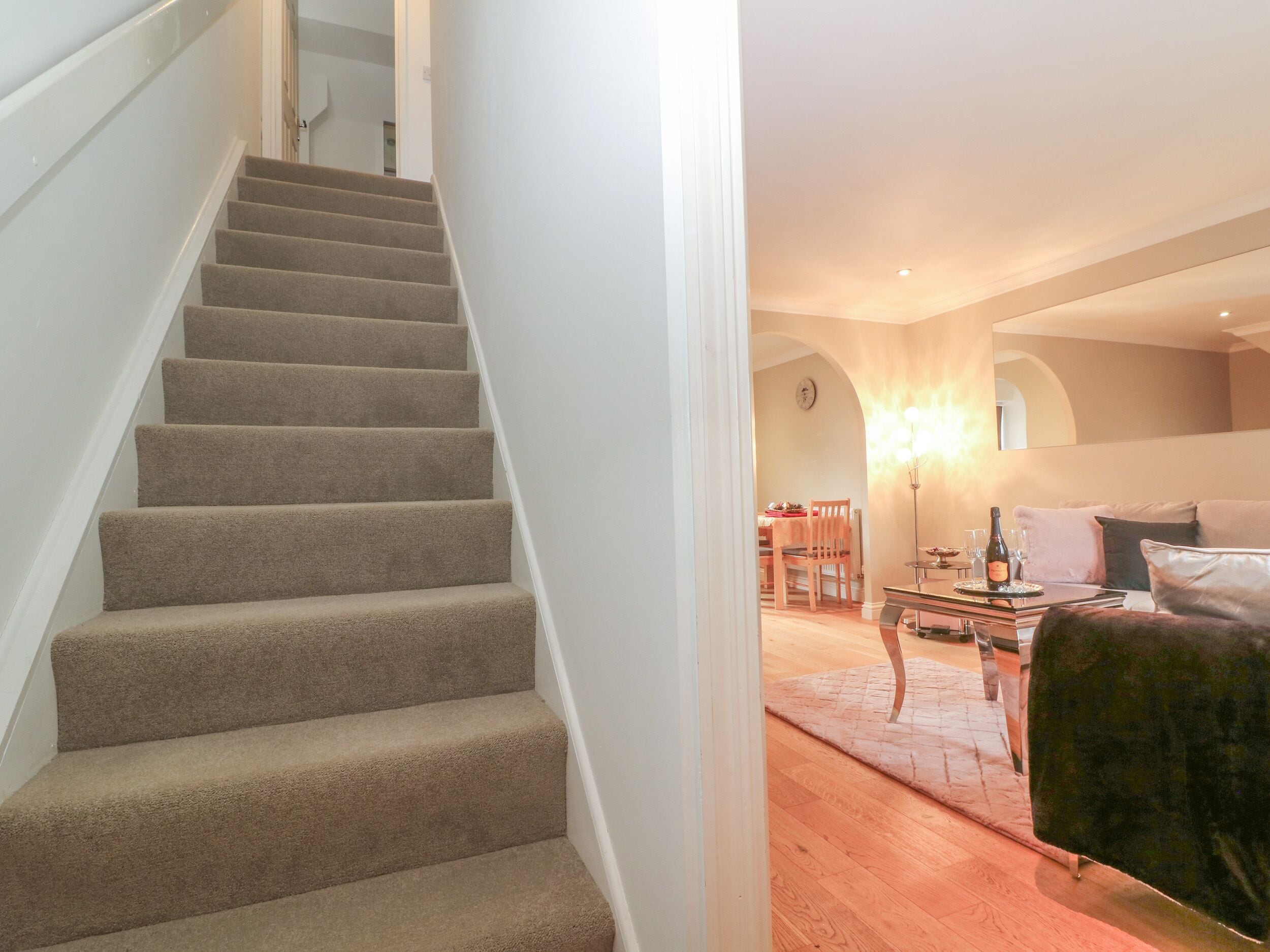 A staircase leading to a dining area with a table and chairs, a sofa, and a lamp.