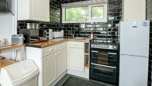 A compact kitchen with white cabinets, a black tiled backsplash, a built-in oven, and a refrigerator. - 98 Cherry Park (Skegness)