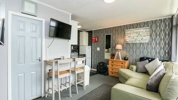 Un espacio habitable compacto con kitchenette, un televisor de pantalla plana sobre el mostrador, un sofá y una pequeña mesa con sillas.