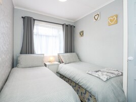 Un dormitorio con dos camas individuales, una mesita de noche con lámpara, una ventana con cortinas y dos adornos en forma de corazón.