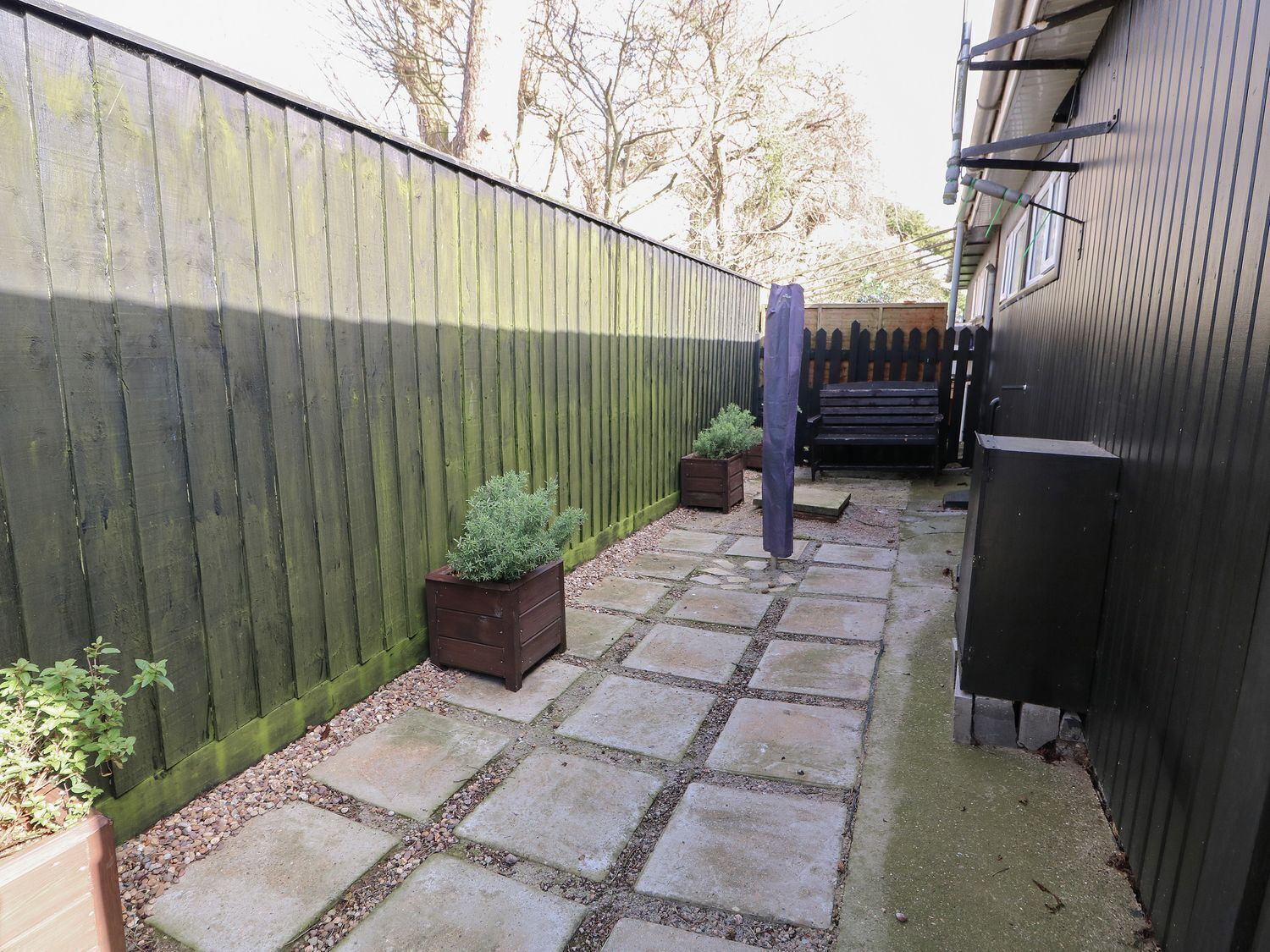 A backyard with a wooden fence, a stone pathway, a wooden planter, and a bench.