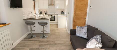 A modern kitchen with a TV, two bar stools, and a wooden door.