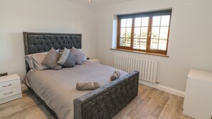 A bedroom with a large bed, a nightstand, a dresser, a radiator, and a window with a view. - Afon Rhos Bach (Caernarfon)