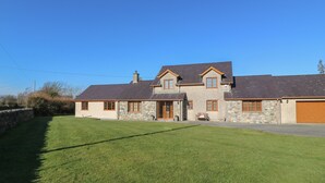 A two-story stone house with a sloped roof, a garage, and a well-maintained lawn. - Afon Rhos Bach (Caernarfon)