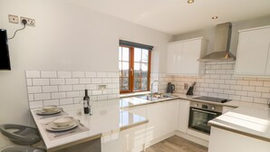 A modern kitchen with white cabinetry, a built-in oven, and a window with a view. - Afon Rhos Bach (Caernarfon)