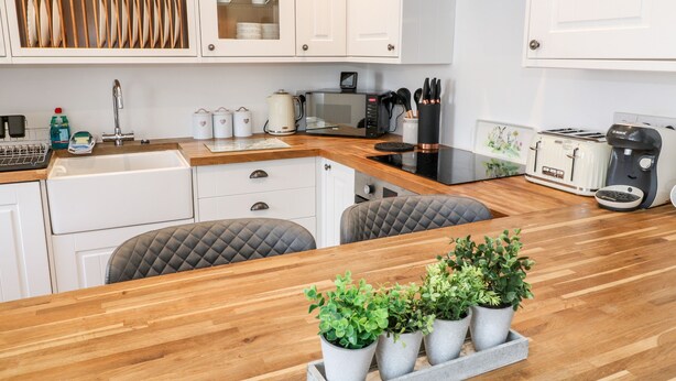 A modern kitchen with white cabinetry, a wooden countertop, a built-in stove, and a coffee maker. - Martingale (Torquay)