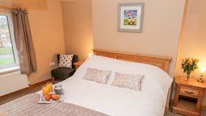 A neatly made bed with a quilt, pillows, and a bedside table with a vase of flowers. - Barnaby Cottage (Yarm)