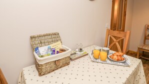 A breakfast setup with a wicker basket, a tray with croissants and orange juice, and a wall clock. - Barnaby Cottage (Yarm)