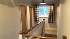 A staircase with white railings and wooden handrails, leading to a room with a window and plaid curtains.