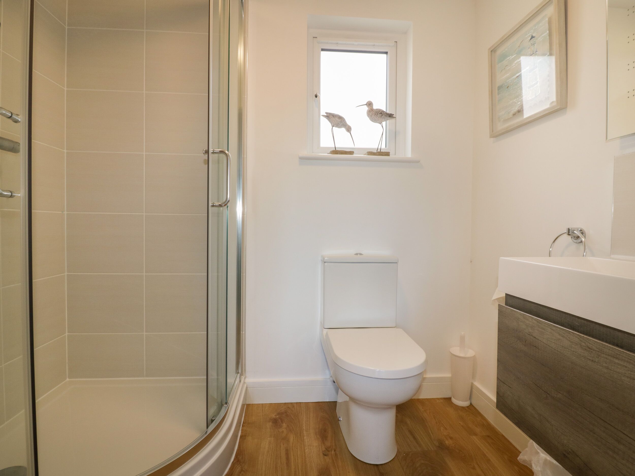 A bathroom with a glass shower enclosure, a white toilet, and a wooden vanity with a sink.