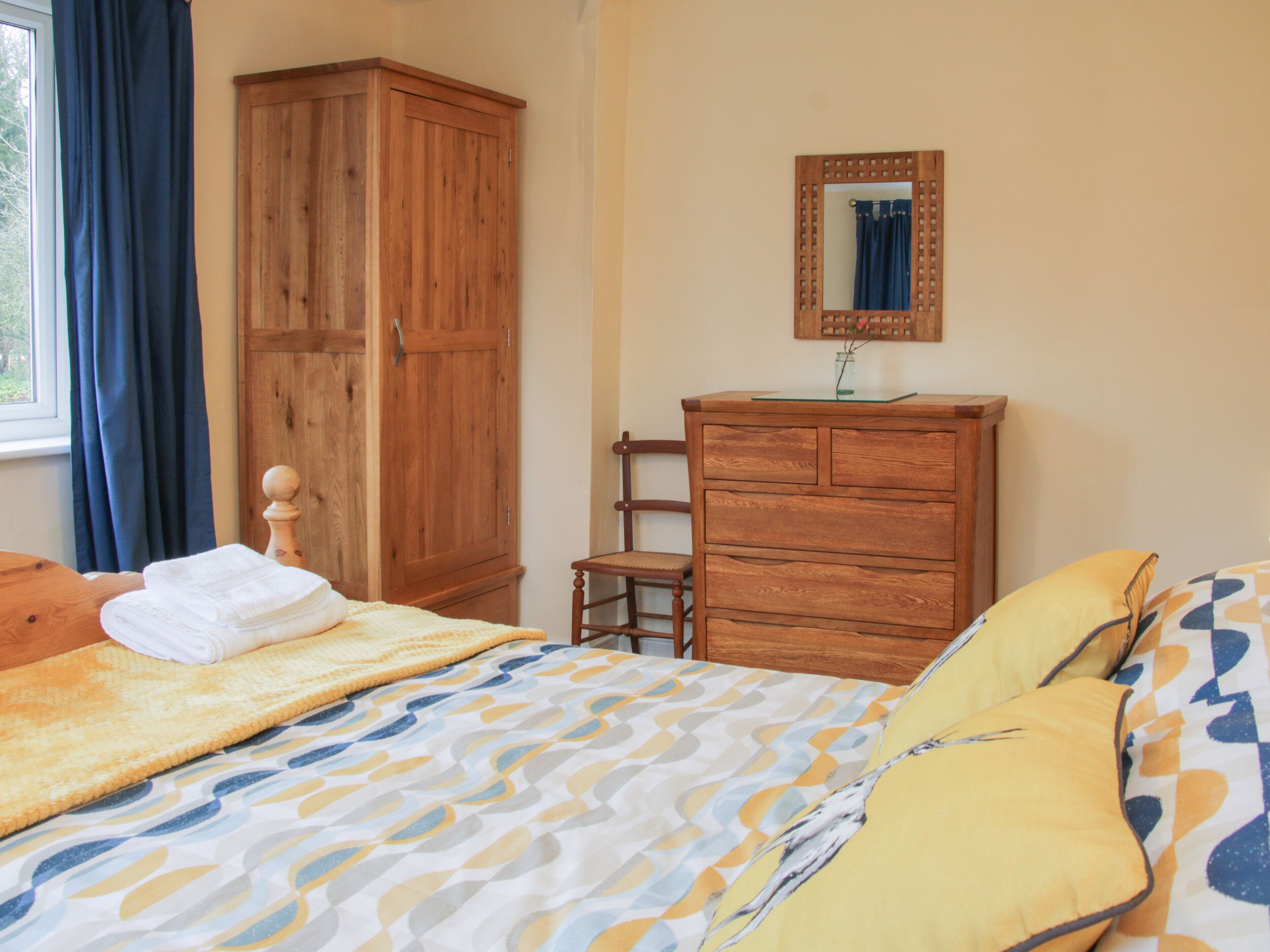 A bedroom with a bed, a wooden wardrobe, a dresser, and a mirror on the wall.