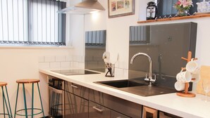 A modern kitchen with a stainless steel sink, a dishwasher, and a built-in oven. There are two stools and a coffee maker on the counter. - Bank House Barn (Shrewsbury)