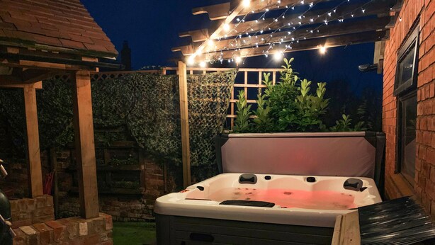 A hot tub in an outdoor patio area with a pergola overhead and string lights. - Bank House Barn (Shrewsbury)