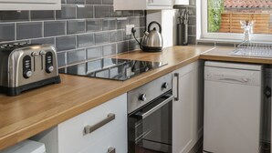 A modern kitchen with a wooden countertop, a kettle, a toaster, an oven, and a dishwasher. - Brinkburn Cottage (Scarborough)