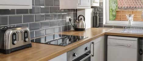 A modern kitchen with a wooden countertop, a kettle, a toaster, an oven, and a dishwasher.
