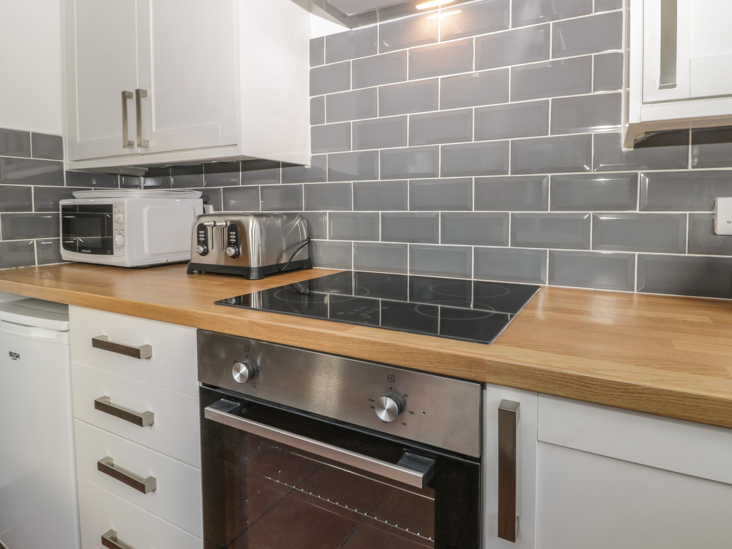 Een moderne keuken met witte kasten, een zwart aanrecht, een inbouwoven, een magnetron en een broodrooster.