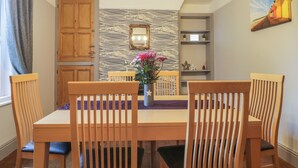 A dining area with a wooden table and chairs, a vase with flowers, a patterned wall, and a painting on the wall. - Brinkburn Cottage (Scarborough)