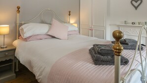 A neatly made bed with a white and pink bedspread, a bedside lamp, and a stack of folded towels on a metal bed frame. - Brinkburn Cottage (Scarborough)