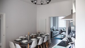 A modern dining area with a dark table set for six, white chairs, and a chandelier. - Oxford House (Llandudno)
