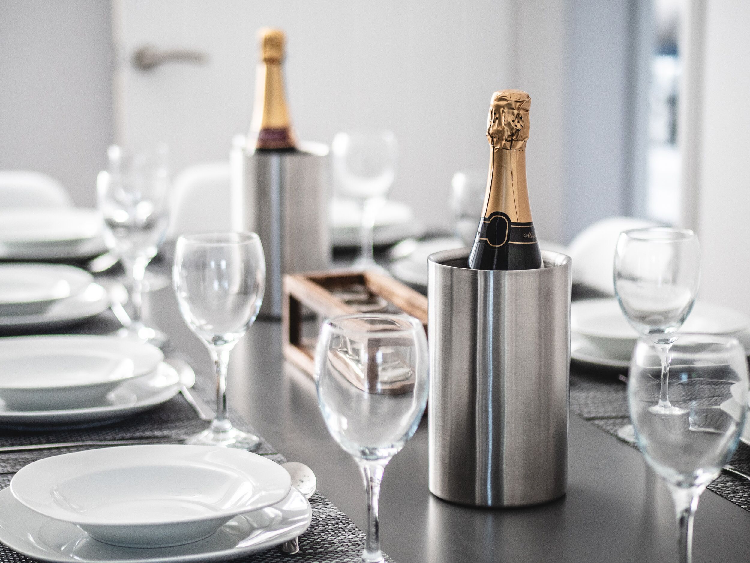 A table set for a formal dinner with champagne bottles in metallic holders, white plates, and clear wine glasses.