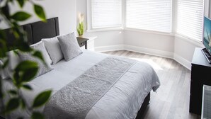 A bedroom with a large bed, white walls, and a window with blinds. - Oxford House (Llandudno)