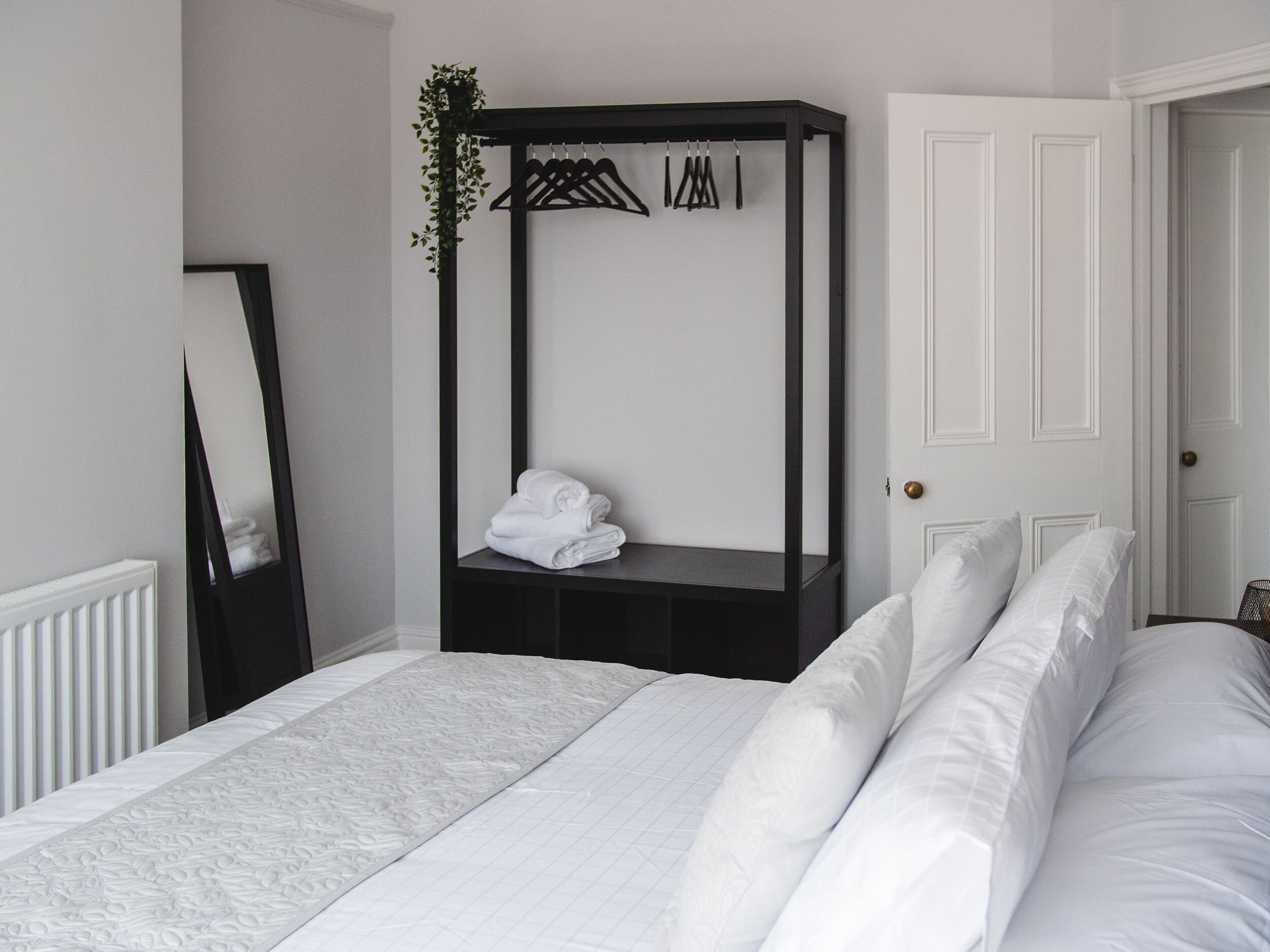 A bedroom with a bed, a bedside table, a wardrobe, a mirror, and a door.