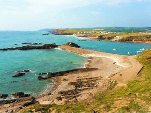 A coastal landscape with rocky terrain, clear waters, and boats. - Silver Crooks (Holsworthy)
