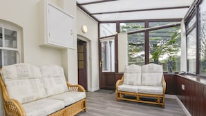 A conservatory with two wicker sofas, wooden flooring, and large windows offering a view of greenery outside. - Silver Crooks (Holsworthy)