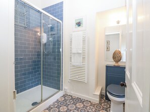 Un baño con cabina de ducha de vidrio, perchero blanco, inodoro y espejo decorativo.