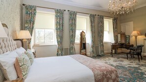A bedroom with a large bed, a dresser, a chair, a mirror, and a chandelier.
